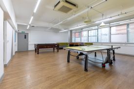 A large room with a ping pong table, a pool table, a table football table, and sofas against the walls.