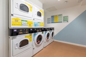 A room with three washing machines and three tumble dryers against one wall.
