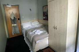 A room with a double bed in one corner and a wardrobe at the foot of the bed.