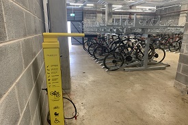 An indoor bike storage space with vertical bike racks. There is an air pump and tool kit facility installed by the wall.