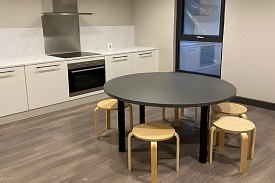 A kitchen/diner with an oven, electric hob, and cupboard storage. There is a circular table with 5 stool placed around it.