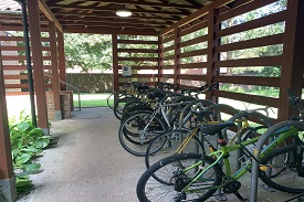 An outdoor covered bike shed with many bikes locked up. 
