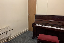 A small music room with an upright piano, a piano stool and a sheet music stand.