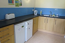 A corner kitchen with storage cupboards, a sink, two refrigerators, a toaster and kettle