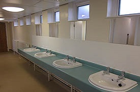 Four sinks in a row, each with its own mirror. At the far end are two wall-mounted radiators