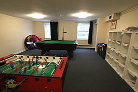 A room containing a table football game, a pool table, recycling bins and shelves