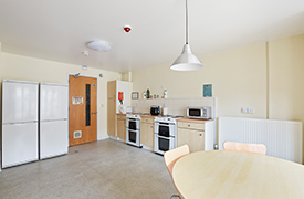 An open plan kitchen/diner with  two ovens, two full-height fridge/freezers, microwave, toaster, kettle, and cupboard units. There is a round dinner table with chairs around it.