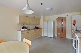 An open plan kitchen/diner with two ovens, two full-height fridge/freezers, microwave, kettle, cupboard units, and a sink. There is a round dinner table with chairs around it.