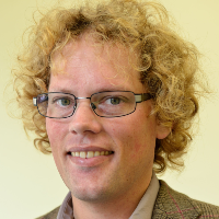 A white man with curly blond hair and glasses, smiling.