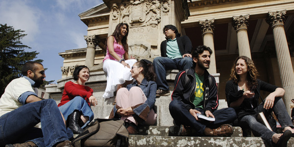 A group of people of different races and genders sit talking by the fountain outside the Victoria Rooms.