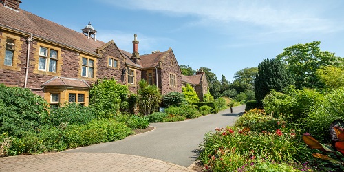 A large two-storey red brick building with a driveway and garden in front of it.