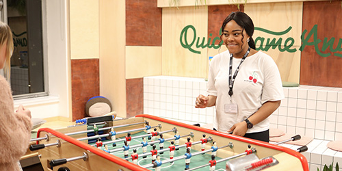 Two women of different races playing table football and smiling.