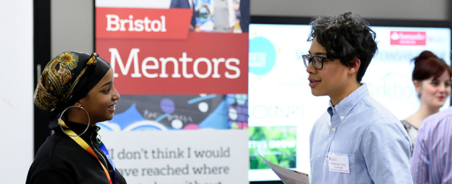 Two people talking to each other in front of a Bristol Mentors branded banner