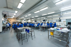 A large dissection room equipped with dissecting tables and tables set up with prosections. On the far side of the room a large number of students are studying in groups.