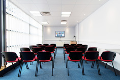 A long brilliantly lit presentation room that is set up with chairs and a large monitor on centre of the far wall.