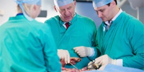 Three surgeons dressed in scrubs are performing surgery in a dissection room. Select to go to the 'Vesalius Clinical Training Centre Courses' page.