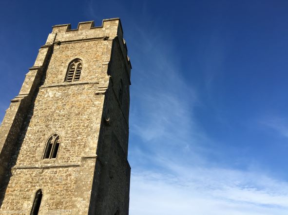 A stone church tower in GLastonbury against a blue sky and clouds