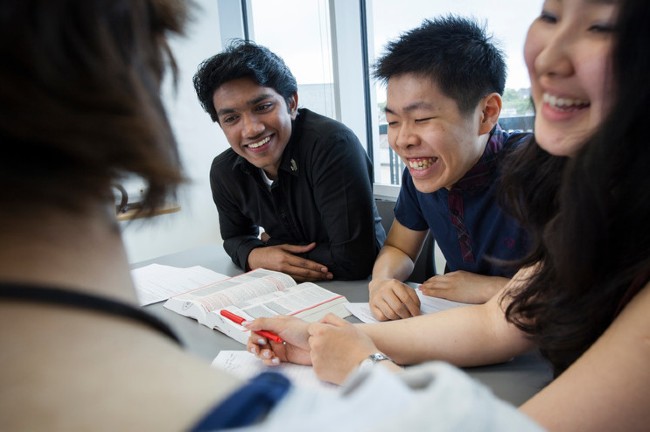 Four laughing students collaborating at desk