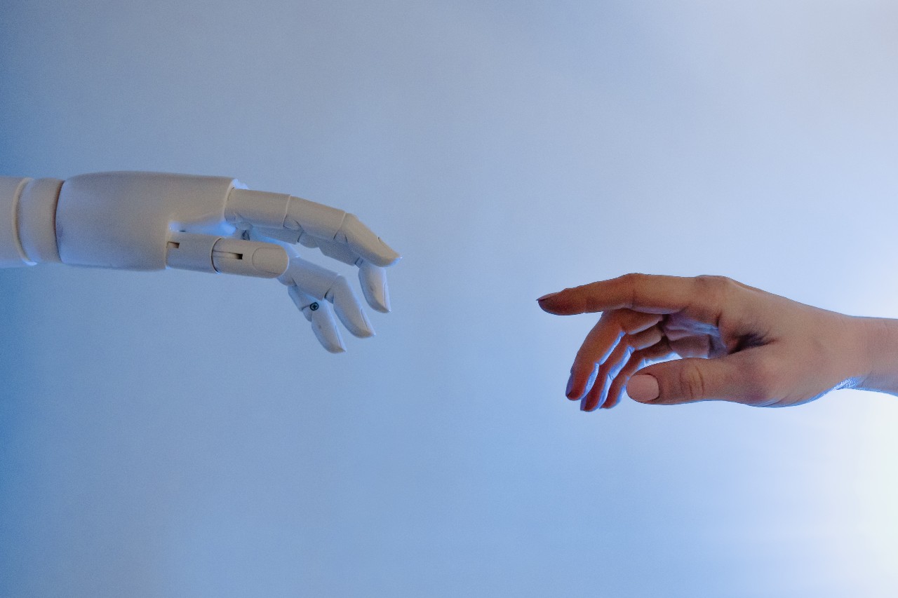 A robot hand stretches out a finger towards a human hand with finger outstretched