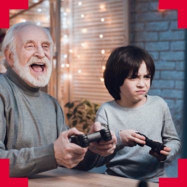a photograph of an older man and a young child holding video game controllers playing together, the old man is laughing while the small boy looks concentrated