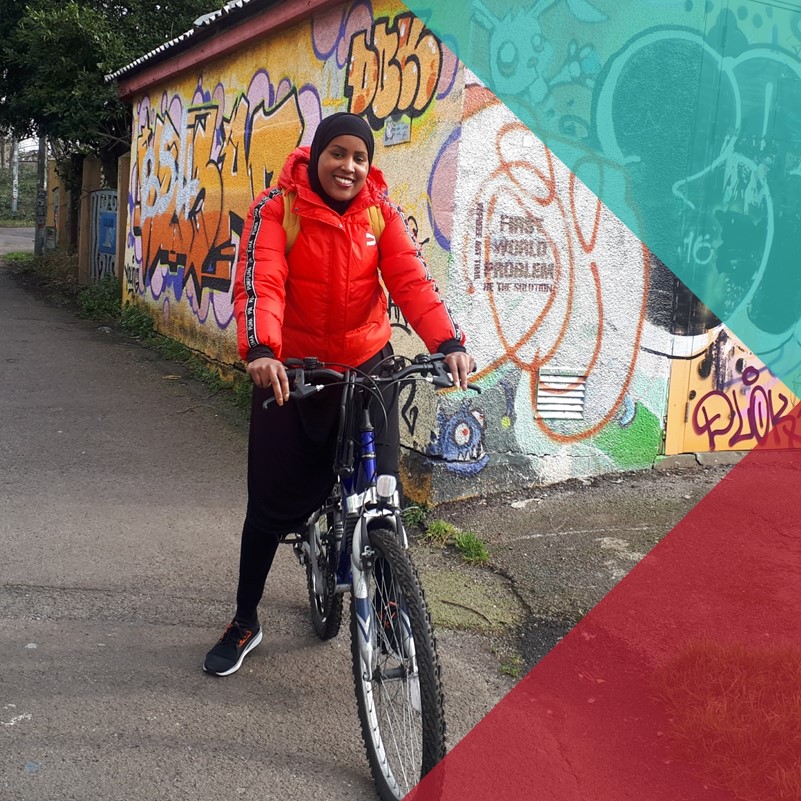 A photograph of a woman on a bike in an urban area participating in the 'How Do You Move' project. 