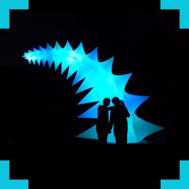 A photo of two silhouetted people in front of a large soft robotic structure created by AirGiants