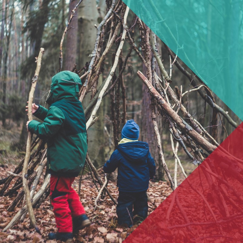 two children building a shelter structure from fallen branches in a forest 