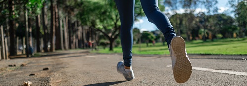 The feet of a woman jogging along a road in the sunshine