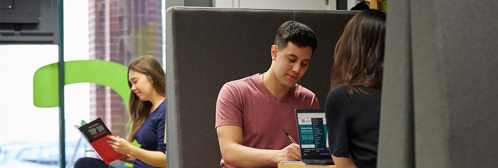 A writing notes in conversation and another student in the background reading a careers book