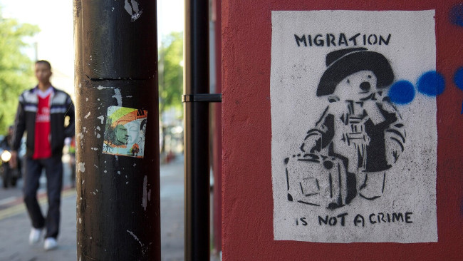 A man walking past a poster of Paddington Bear containing the words 'Migration is not a crime'