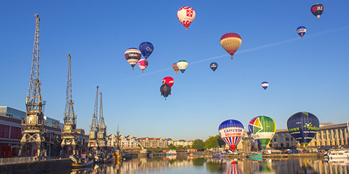 Sixteen hot air balloons flying over and taking off from Bristol Harbour on a sunny day