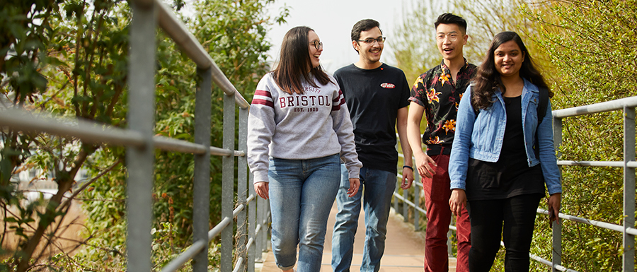 A group of students outside, smiling and walking along a pathway between green trees