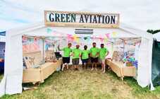 Five volunteers in bright green shirts stand under a tent with a sign 'Green Aviation' at the Glastonbury Festival