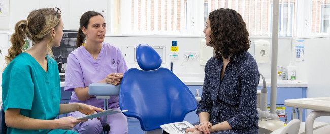 A patient talking to two dental professionals in a dental treatment room
