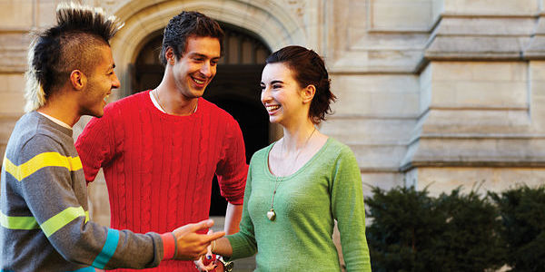 A woman and two men talking and laughing outside an old building. 