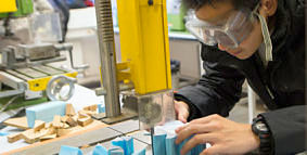 Student in protective goggles using workshop equipment