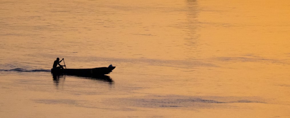 A fisherman travels across Lake Victoria in his canoe at sunset