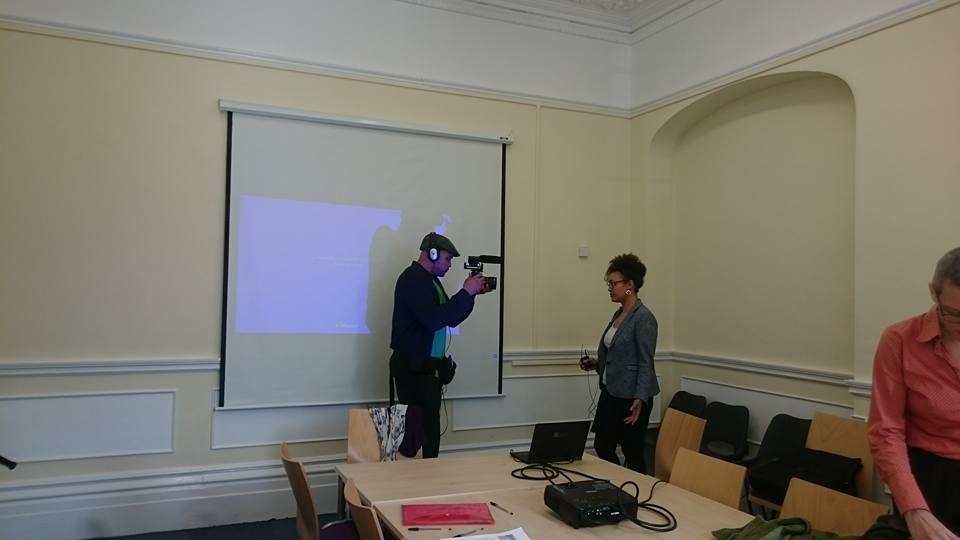 Photo of 3 people in a seminar room with a projector screen
