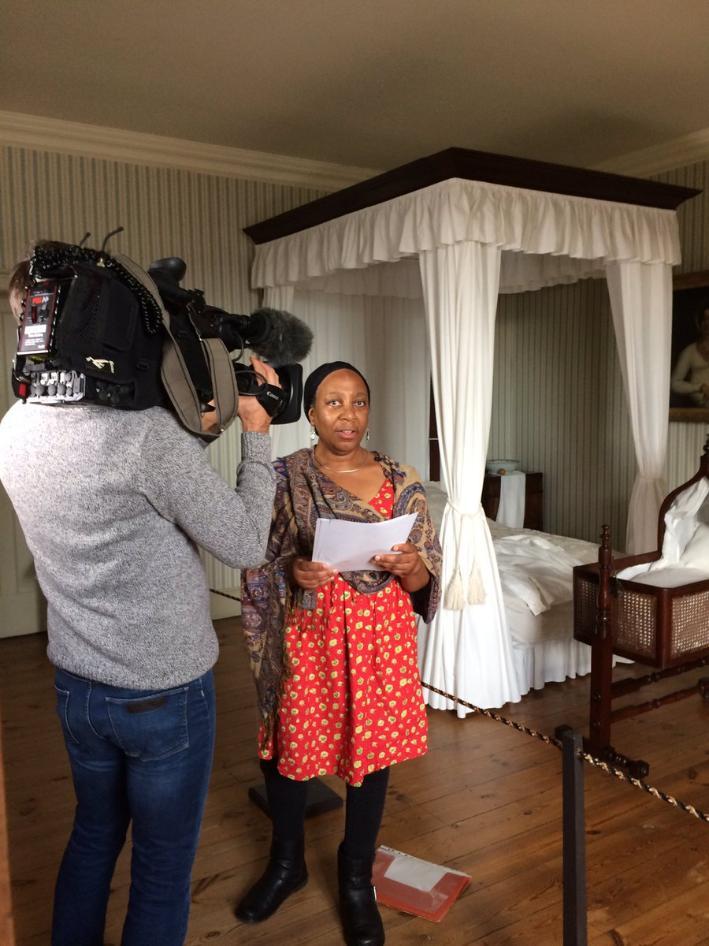 Photo of woman standing in Georgian House bedroom reading and being filmed by cameraman