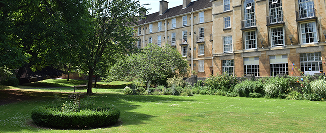 A large lush green lawn with hedges around the edge. There is a large old building behind the lawn