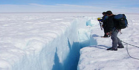 Two people stood next to a crevasse in an icy landscape.