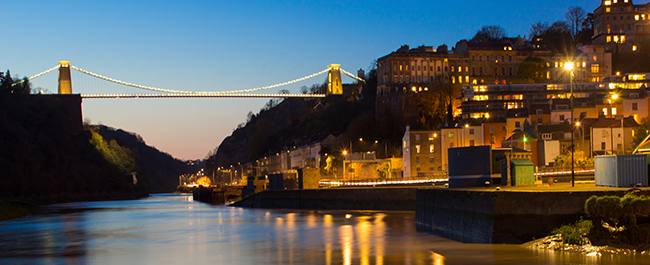 Clifton Suspension Bridge and surrounding buildings are illuminated in the night sky.