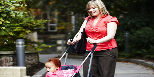 A white woman smiling and walking with a child in a pushchair.