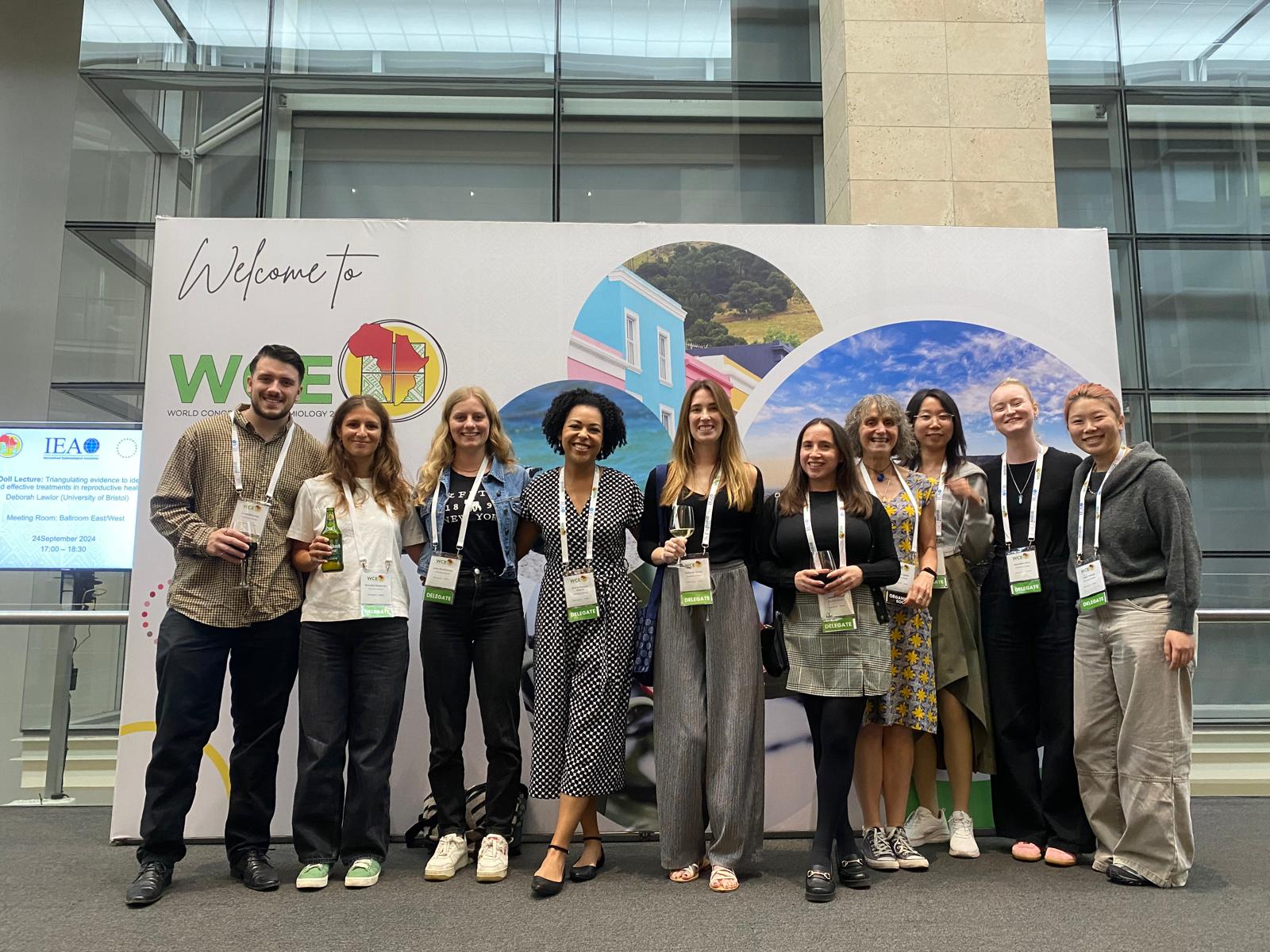 A colour picture of people lined up in front of a colourful poster saying welcome to World Congress of Epidemiology.