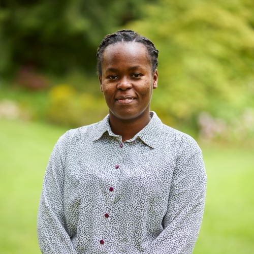 A student in a white patterned shirt. The background is a blurred garden.