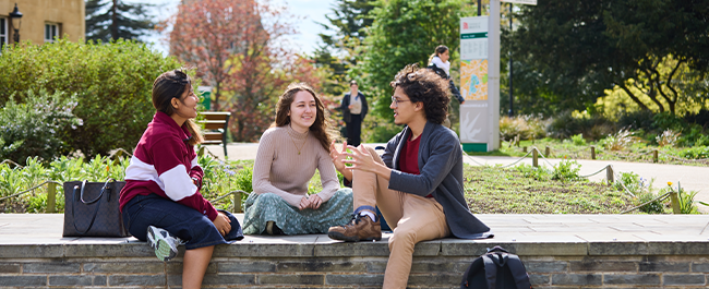 Three students sat together on a wall.