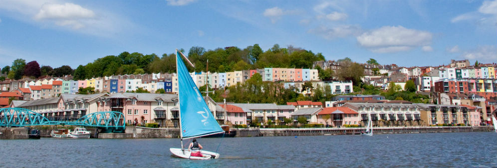 A dinghy boat sailing past the colourful houses at Bristol