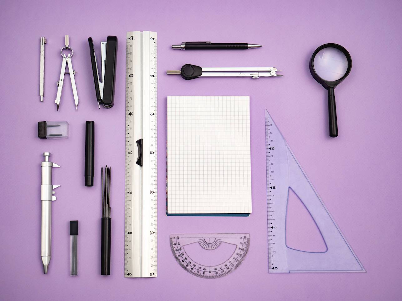 An array of stationary and tools for drawing and design on a pink background.