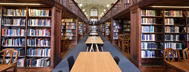 Shows one of the wings of the Wills Memorial Library. A large wood panelled library on two floors with a very decorative ceiling, with book shelf alcoves with large study desks.