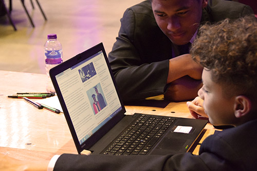 BAME child and adult looking at laptop with pictures of BAME graduates